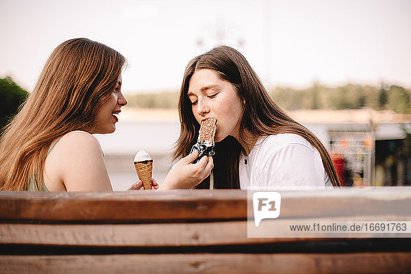 Junge Frau füttert ihre Freundin auf einer Bank in der Stadt mit Eiscreme