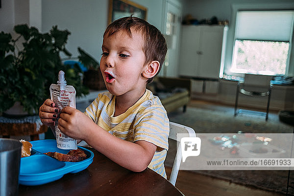 Kleines Kind freut sich über einen gepressten Joghurt am Tisch