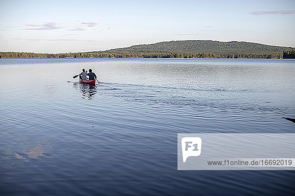 Canoe paddled by two people heads into the distance on lake in Maine