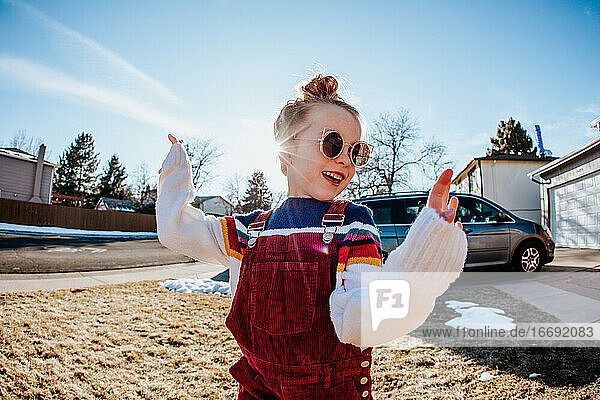 Close up of young girl dancing in front yard with sunglasses on