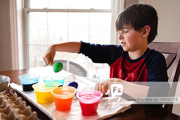 Ein Junge taucht ein Ei in eine Schale mit Farbstoff  um es für Ostern zu färben.