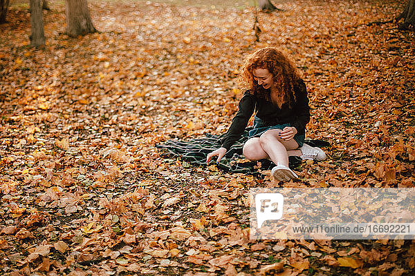Glückliche junge Frau auf einem Feld mit trockenen Blättern im Herbst sitzend