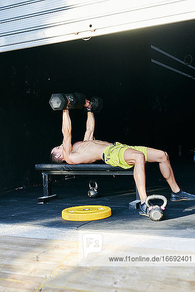 Hemdfreier fitter junger Mann  der in einer Garage mit Hanteln trainiert