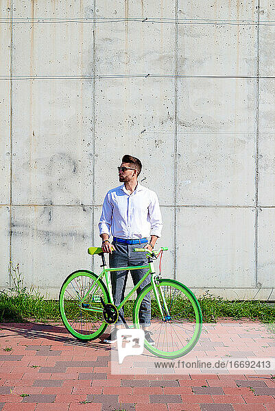 Junger bärtiger Mann mit Sonnenbrille steht mit Fahrrad im Freien