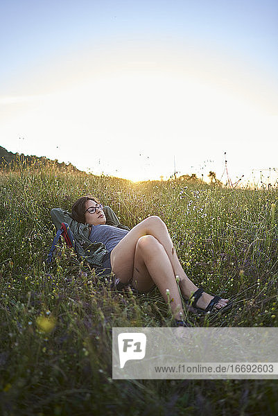Frau auf einer Wiese liegend bei Sonnenuntergang.