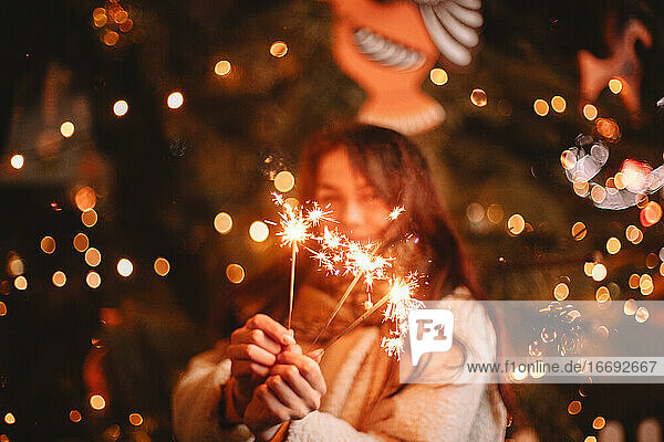 Teenager-Mädchen mit Wunderkerzen vor einem leuchtenden Weihnachtsbaum