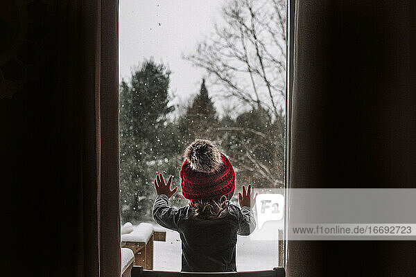 Little girl looks out the window during a snow day in the winter