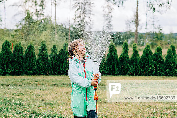girl spraying water in her face with a hose in the yard in summer