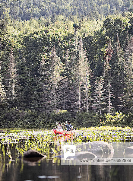 woman and african american male paddle in red canoe on lake in Maine