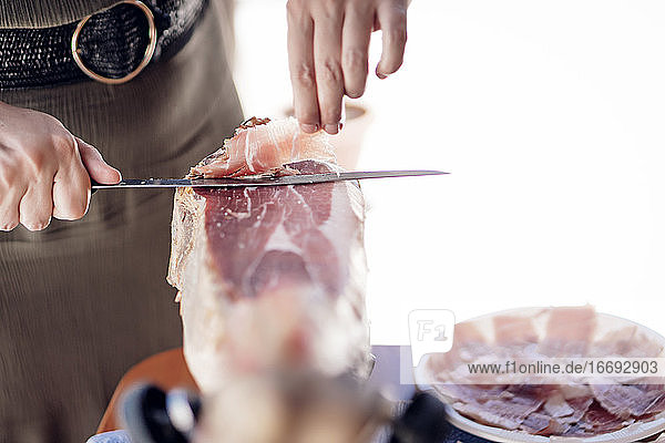 Frau schneidet iberischen Schweineschinken mit einem Schinkenhalter und einem Messer