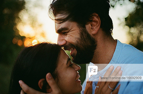 Mann lacht und küsst Frau im Freien bei Sonnenuntergang
