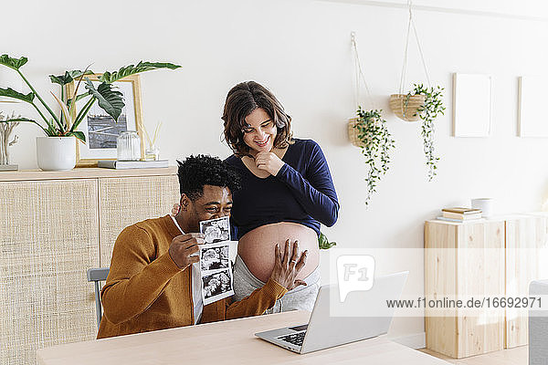 Ehemann und schwangere Frau sehen sich Ultraschallbilder ihres Babys an. Unter