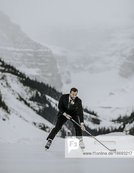 Just married groom skates with hockey stick on Lake Louise  Alberta