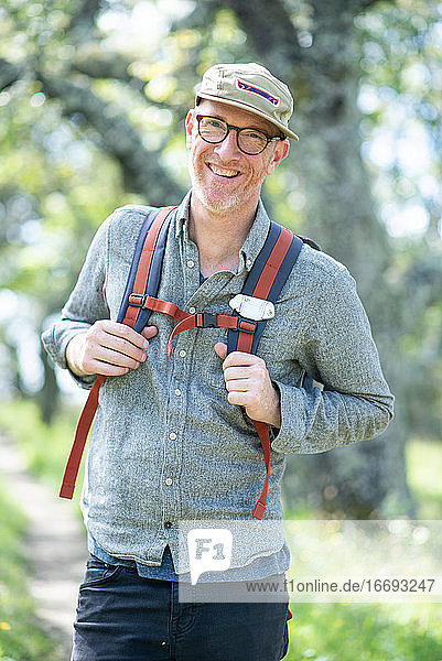 Porträt eines lächelnden Wanderers mit Hut  Brille und Rucksack im Freien