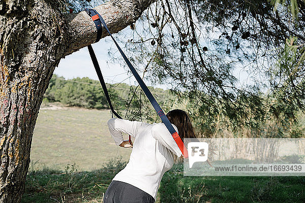 TRX sport team. Young woman doing exercises outdoors in a park. Strap
