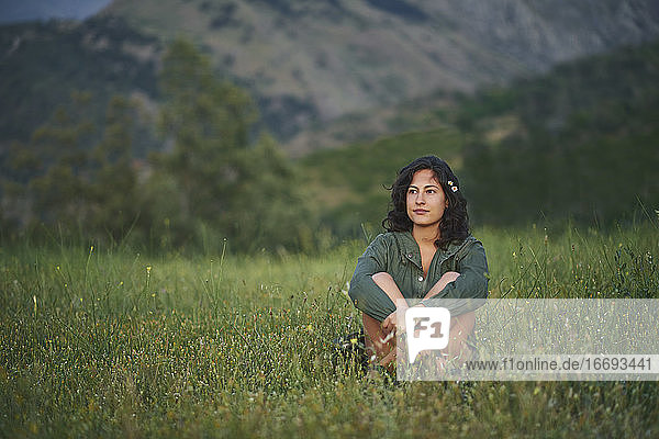 Portrait of a young woman sitting in a meadow at sunset. The sun illuminates her face.