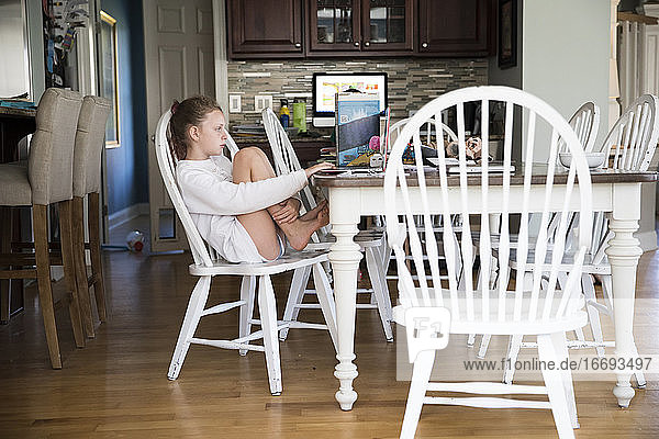 Young Girl Sits at Kitchen Table Doing School Work on Laptop Computer