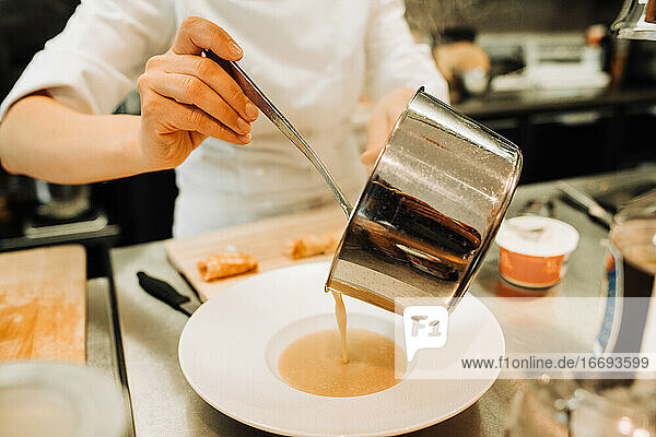 Koch gießt Suppe in Teller bei der Arbeit in der Restaurantküche