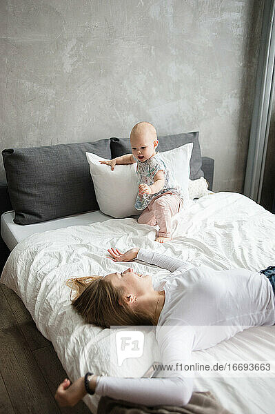 Junge Frau und kleines Mädchen liegen auf dem Bett und lächeln beim Spielen. Kindermädchen.