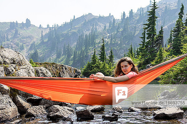 Woman is peeking out of a hammock at the alpine lake on local vacation