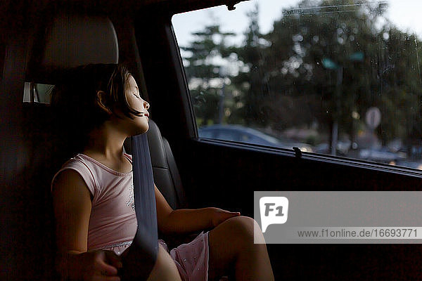 A beautiful little girl wearing seat belt sleeps in a car at twilight