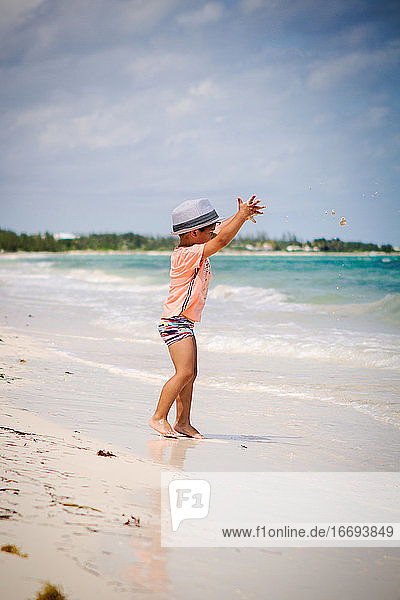 Kleiner Junge mit lockigem Haar wirft Sand an einem Strand in der Karibik