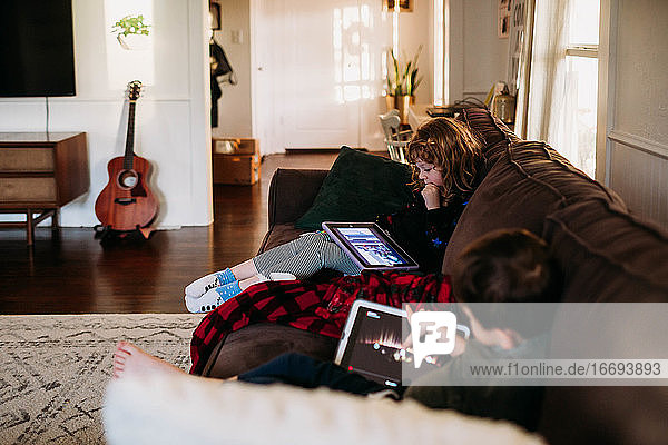 Young sister and brother using tablets at home on sick day