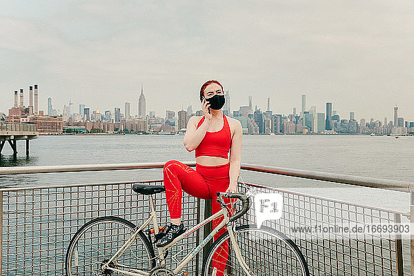 Junge Radfahrerin telefoniert mit ihrem Fahrrad an der Uferpromenade von Brooklyn