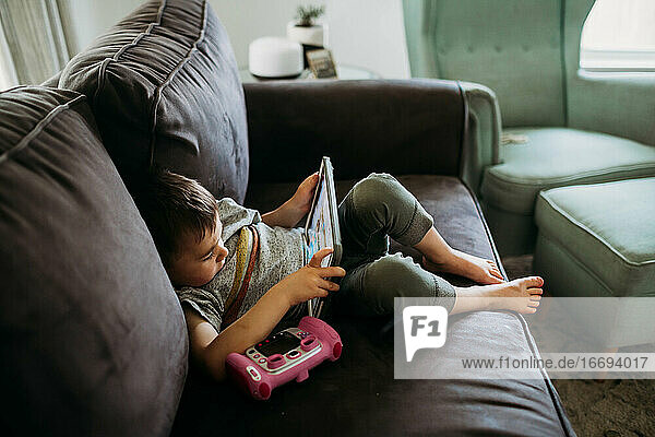 Kleiner Junge sitzt auf der Couch und spielt ein Lernspiel auf einem Tablet