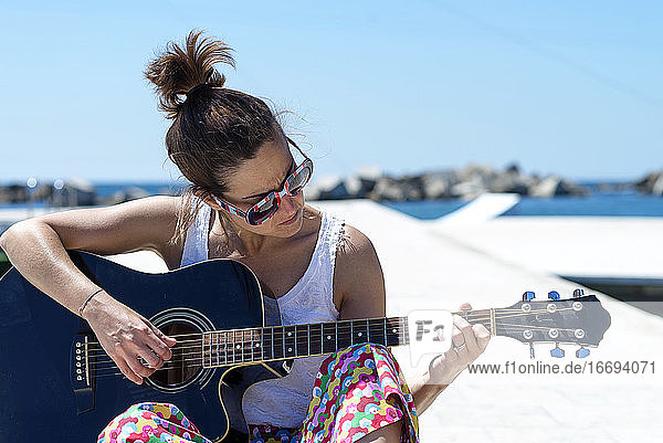 Junge Frau sitzt auf einem Boden und spielt Gitarre