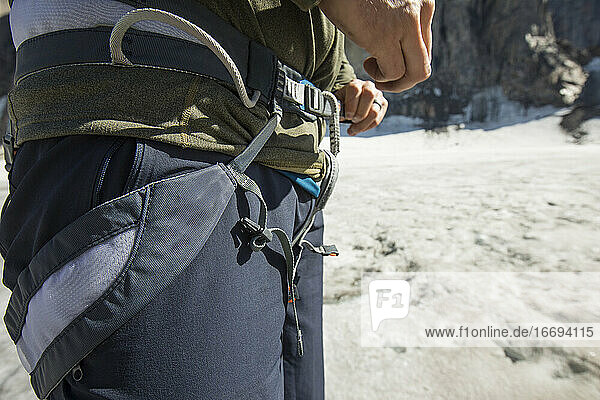 Mountain climber tightens his climbing harness prior to climbing.
