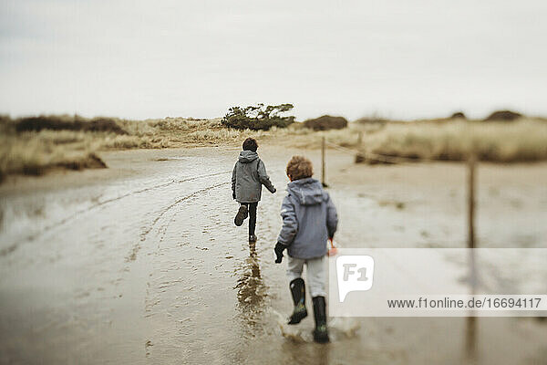 Two boys in winter running through puddles on sand dune saltmarsh