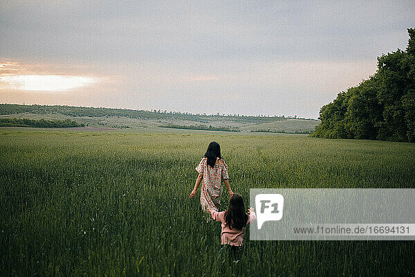 mother and daughter walking in field at sunset