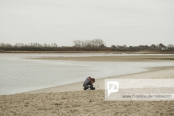 Cute boy on sandy beach kneeling down to study findings