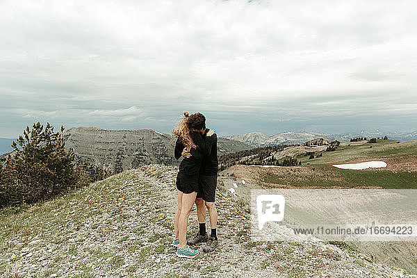 engaged couple in all black embrace hug on windy ridge top in wyoming