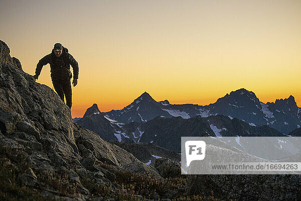 Ein Wanderer geht nach Sonnenuntergang mit einer Stirnlampe einen Bergweg entlang.