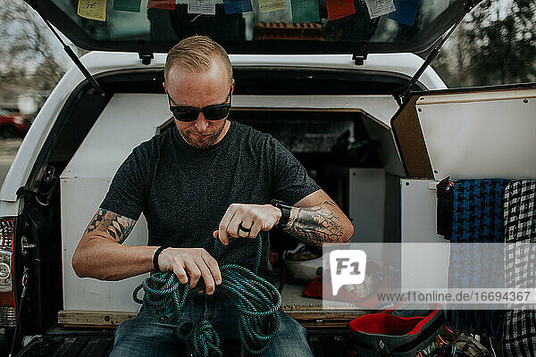 man sitting on back of truck preparing rock climbing ropes