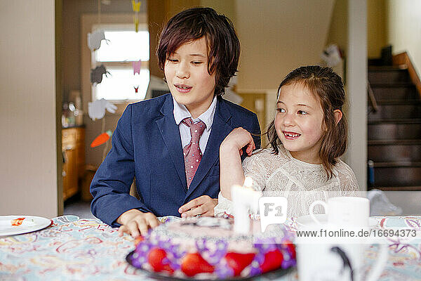 two smiling children sit at a table in front of lit birthday cake