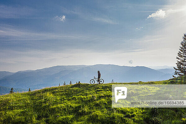 Mountainbiker auf seinem Fahrrad auf einem grünen Hügel an einem sonnigen Tag