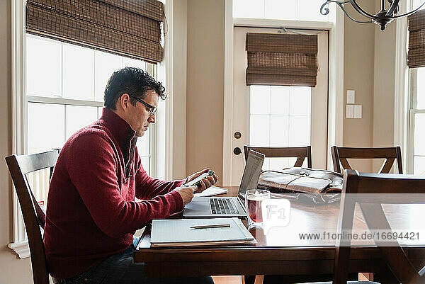 Mann mit Brille arbeitet von zu Hause aus an einem Computer am Esstisch.