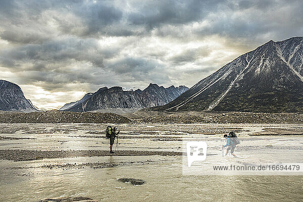 Zwei Rucksacktouristen überqueren einen verzweigten Fluss auf einem Bergpass.
