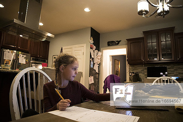Blondes Mädchen am Küchentisch erledigt Schularbeiten am Tablet-Computer