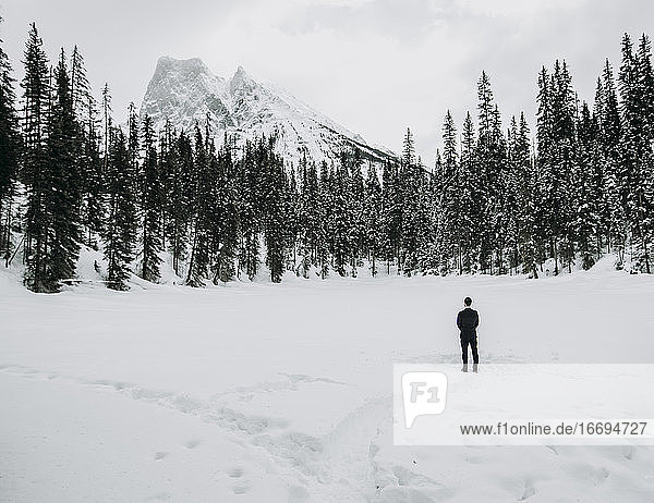 einsamer Mann im Anzug steht allein auf einem schneebedeckten See mit Bergen