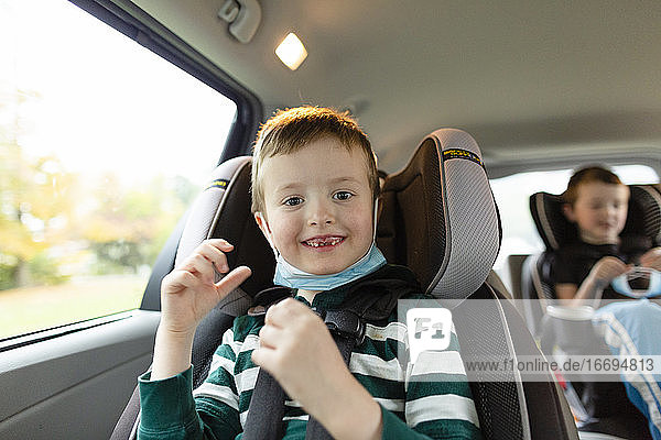 Elementary Age Boy Smiling While Sitting in Car With Face Mask