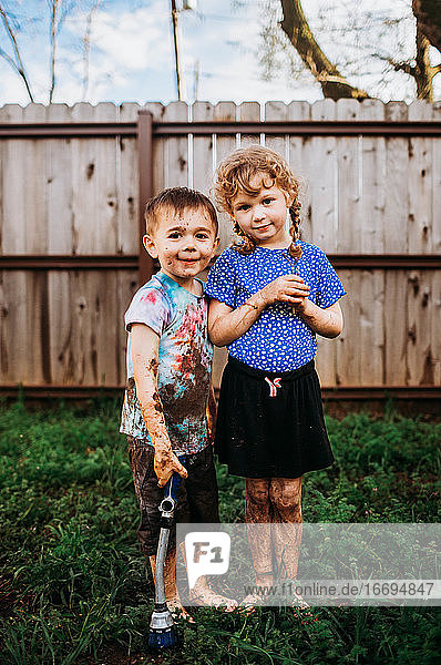 Two young kids playing in muddy backyard in spring