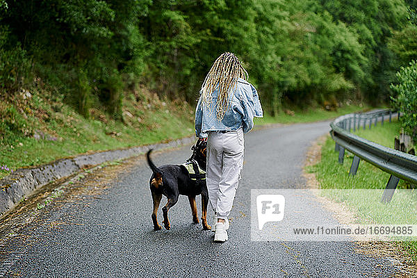 Junge Frau mit blondem geflochtenem Haar  Jeansjacke und weißer Jeans  die an einem regnerischen Tag mit ihrem Hund spazieren geht