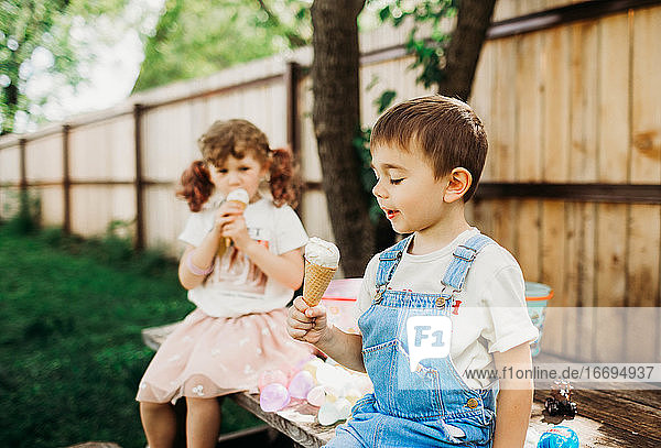 Zwei junge Kinder  die draußen sitzen und eine Eistüte essen
