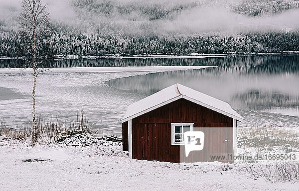 traditionelle rote Hütte mit Blick auf einen schneebedeckten See und Wald