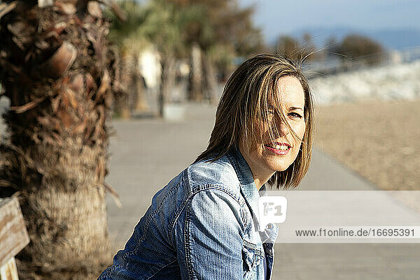Lächelnde Frau sitzt auf einer Bank in der Nähe des Strandes und schaut in die Kamera