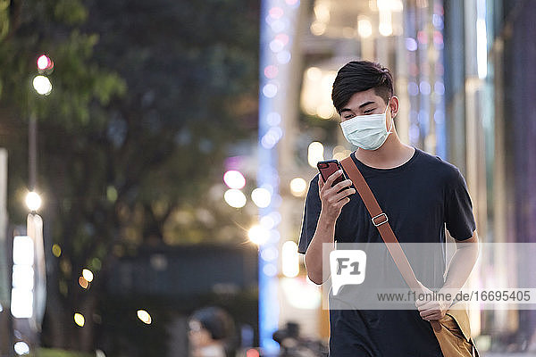 Young man with protective face mask using mobile phone in city s